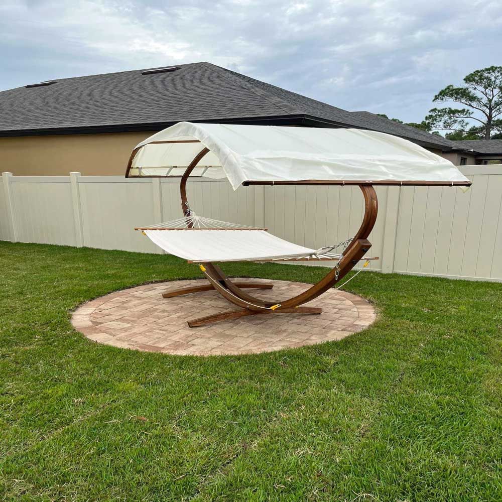 A hammock with a canopy is sitting in the grass in front of a house.