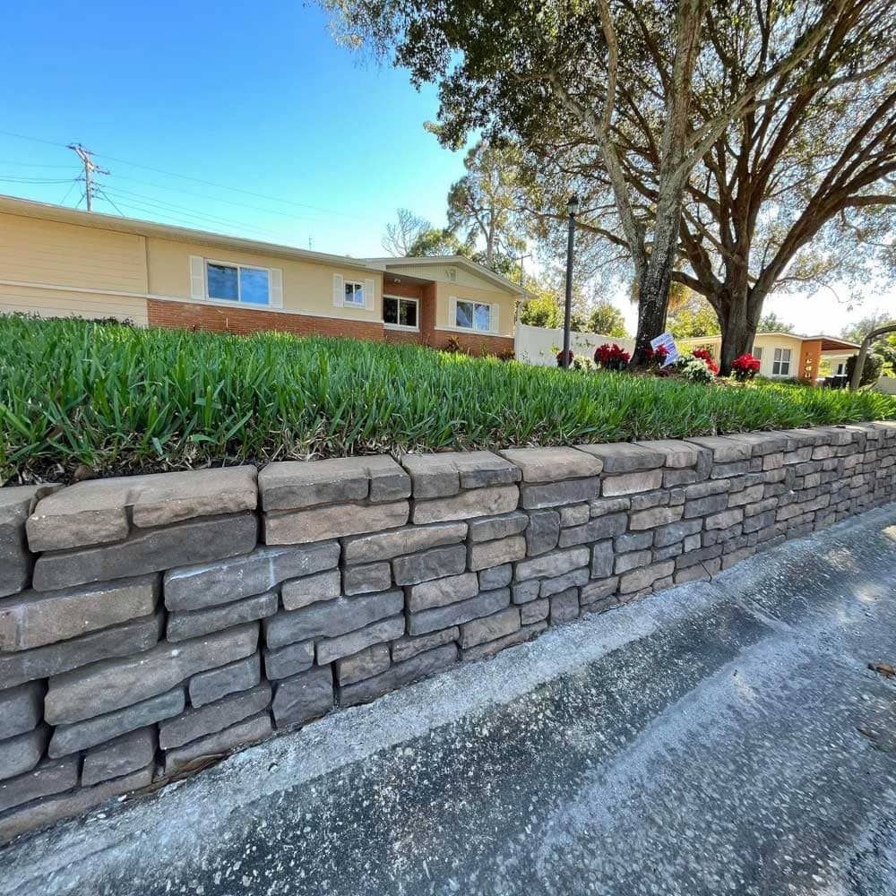 A stone wall surrounds a lush green lawn in front of a house.