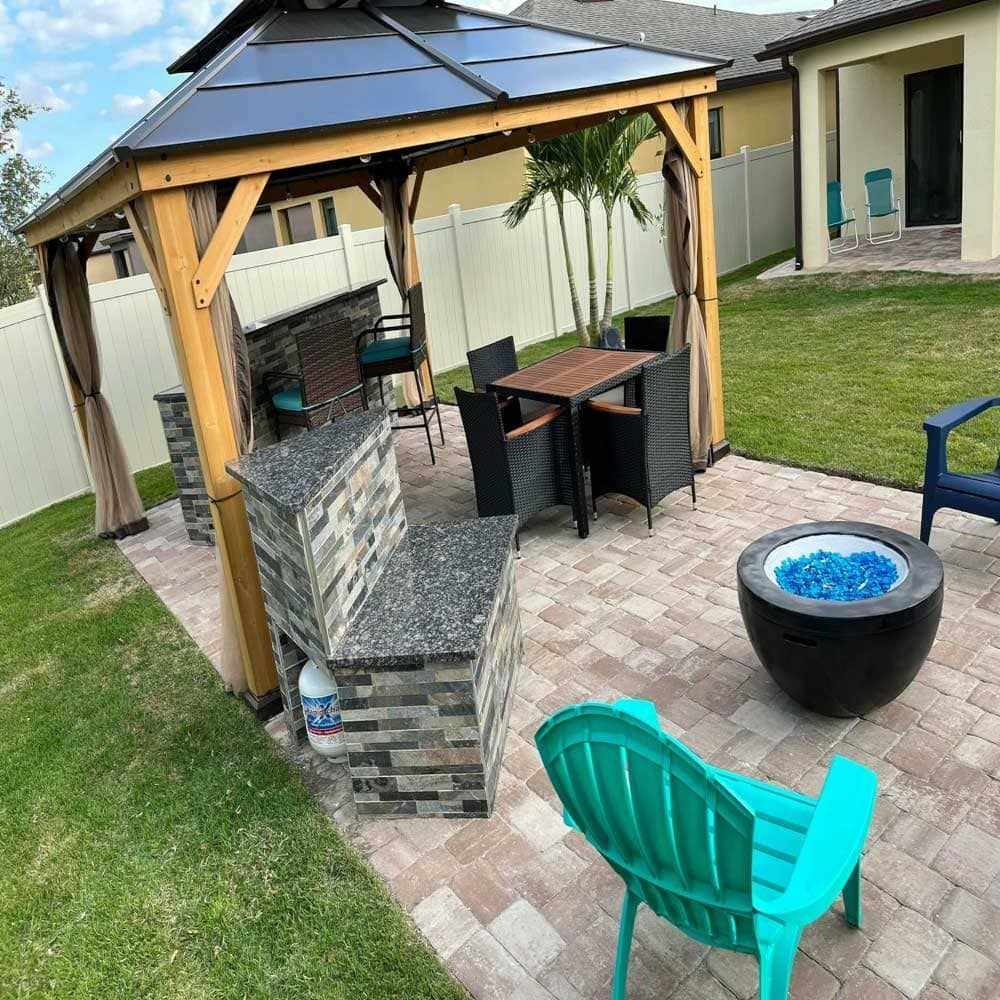 A patio with a gazebo , chairs , a table and a fire pit.
