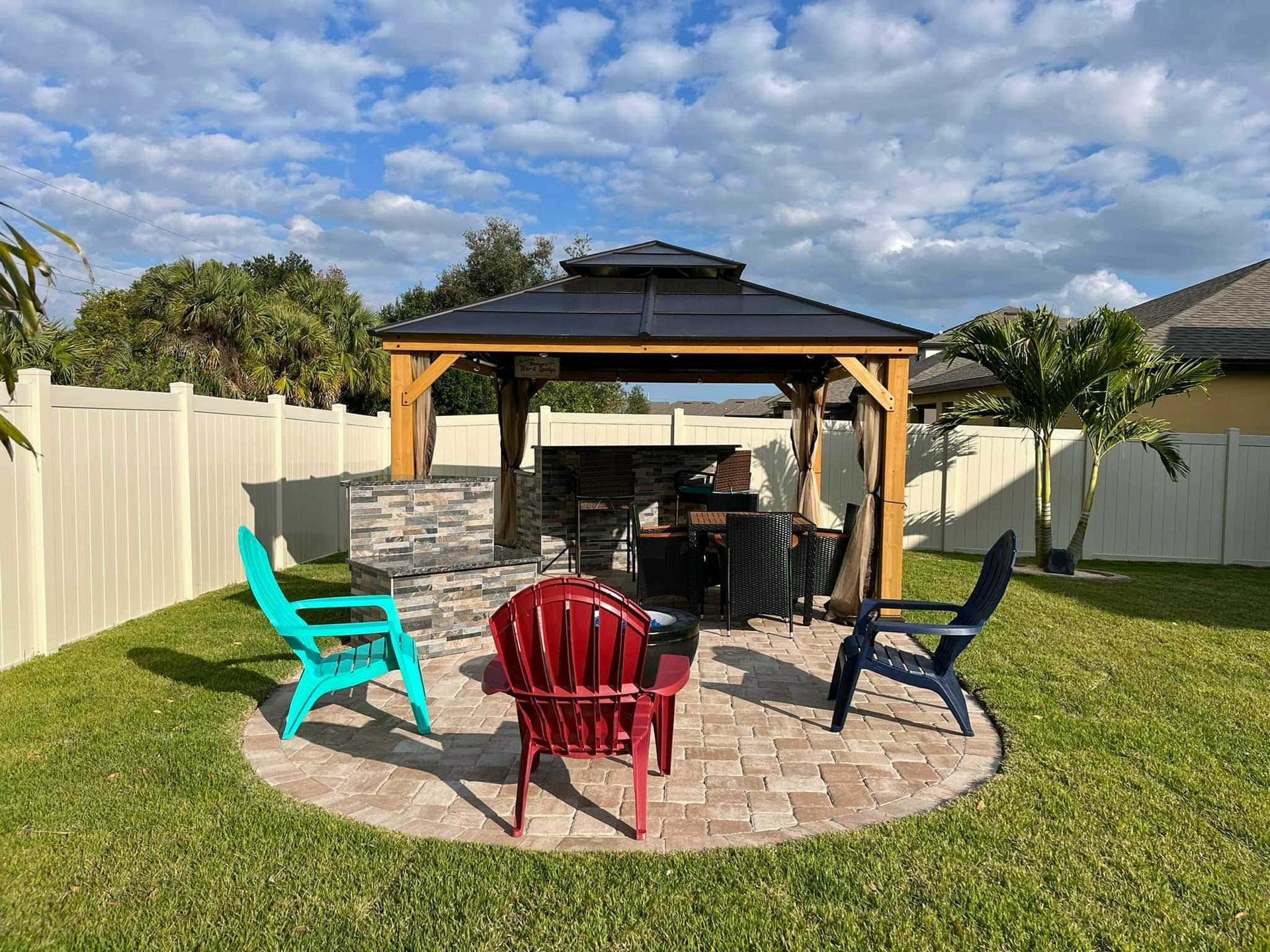 A gazebo with a fire pit and chairs in a backyard.