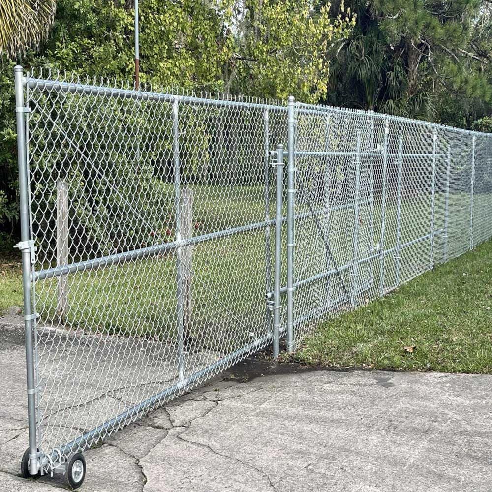 A chain link fence with wheels is sitting on the side of a road.