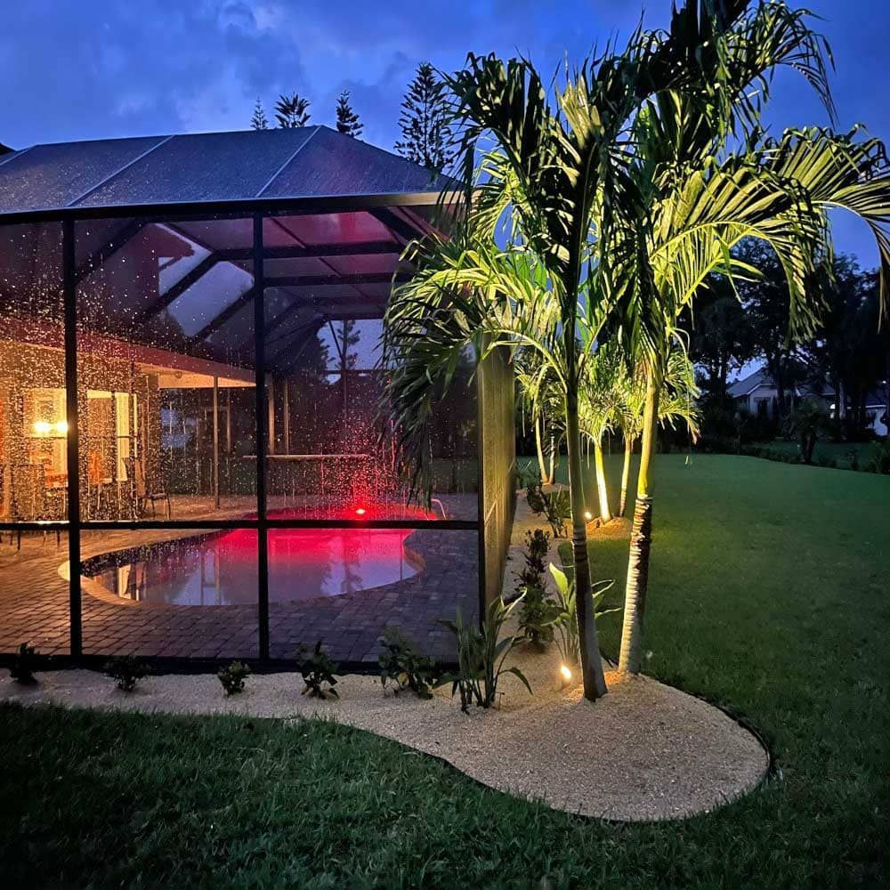 A screened in swimming pool is lit up at night.