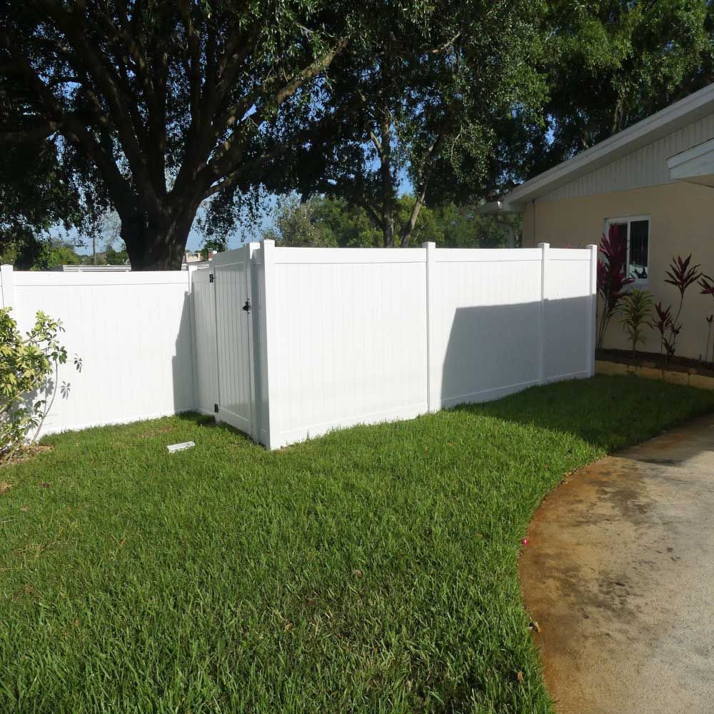 A white fence surrounds a lush green yard in front of a house