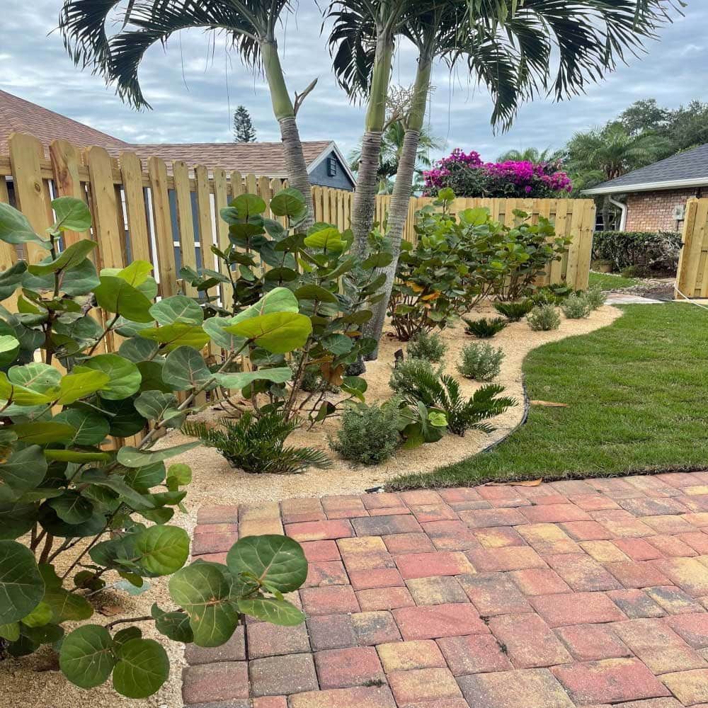 A brick walkway leading to a backyard with a wooden fence and lots of plants.
