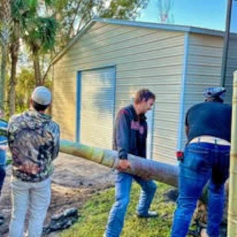 A group of men are standing in front of a shed carrying a large pipe.