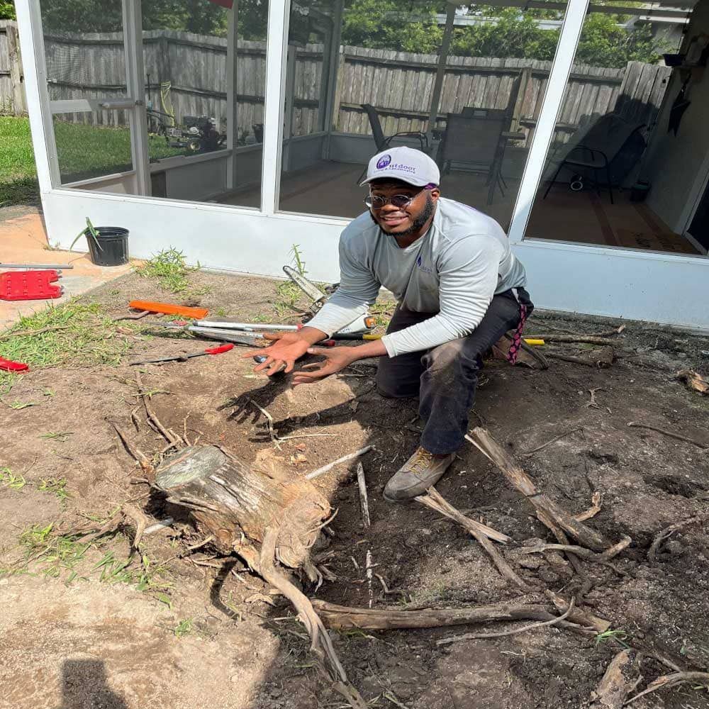 A man is kneeling down next to a large tree stump.
