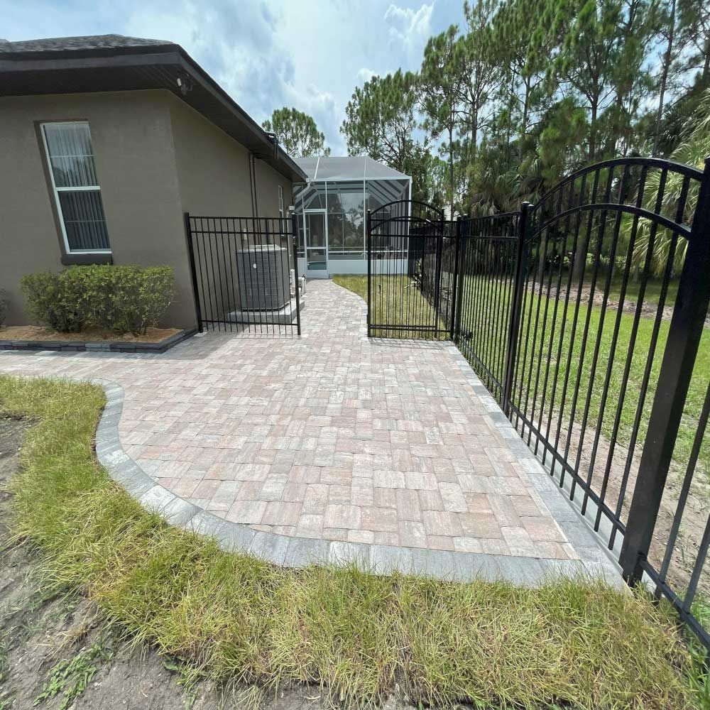 A brick walkway leading to a house with a fence and a pool.