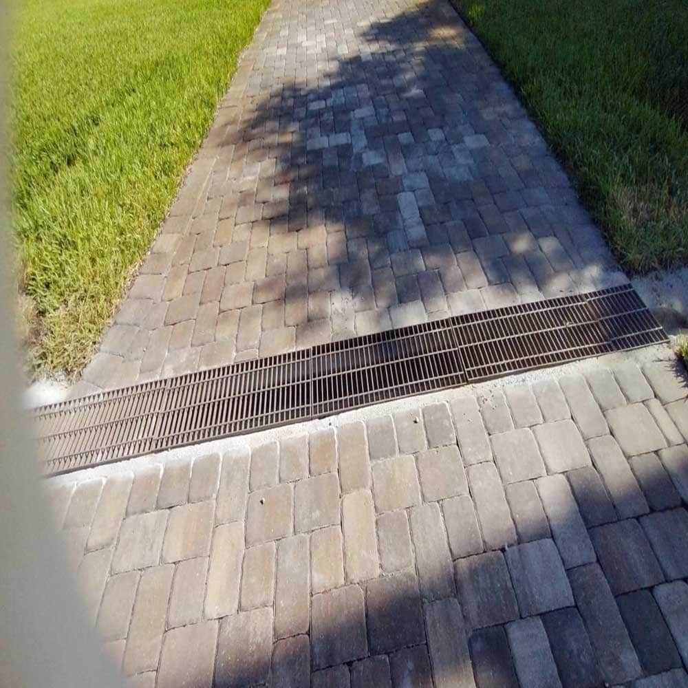 A brick walkway with a metal grate on the side of it.