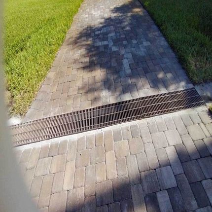 A brick walkway with a metal grate on the side of it.