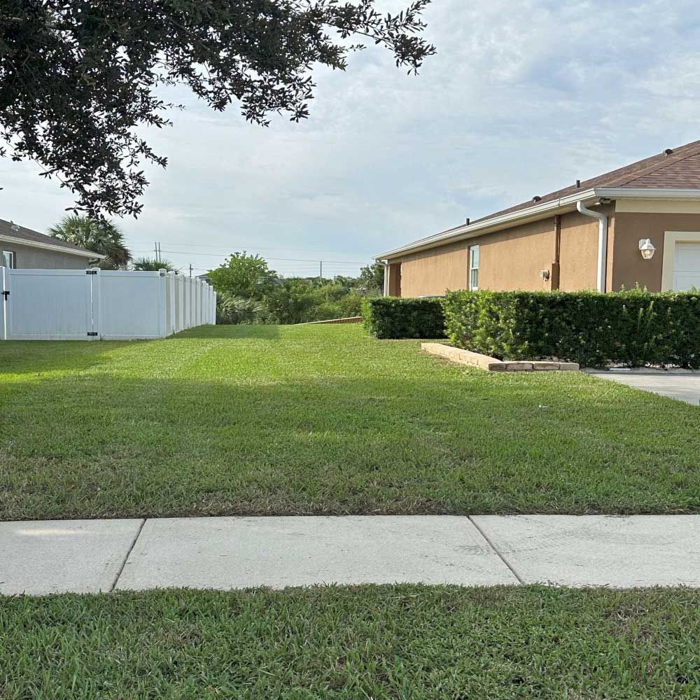 A lawn with a white fence and a house in the background