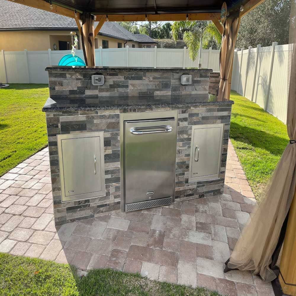 A brick and stainless steel outdoor kitchen with a gazebo in the backyard.