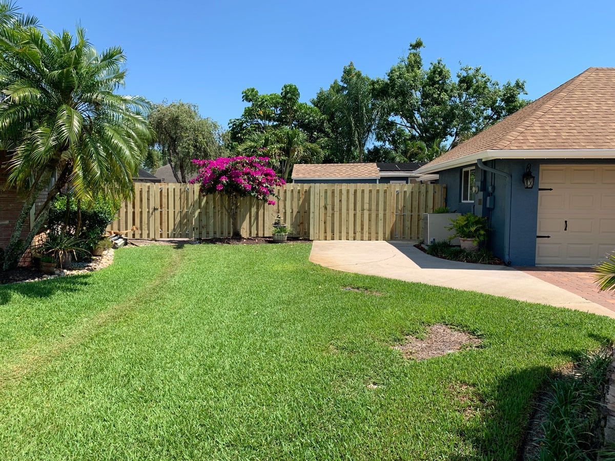 A wooden fence surrounds a lush green lawn in front of a house.