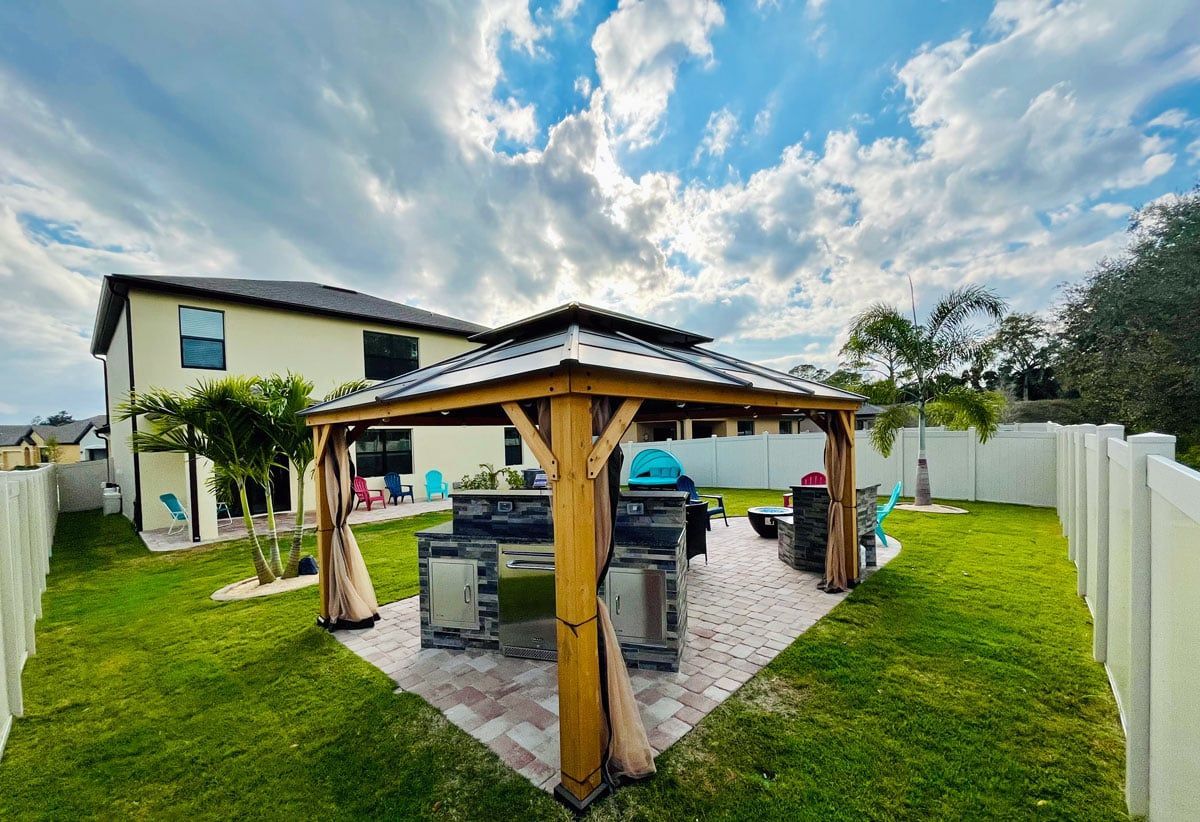 A gazebo with a grill in the backyard of a house.