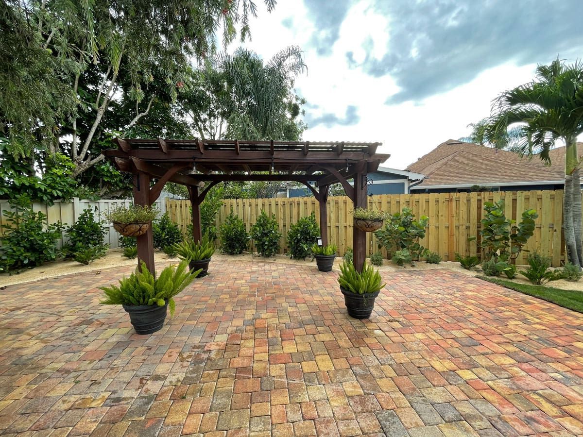 A brick driveway with a pergola and potted plants.
