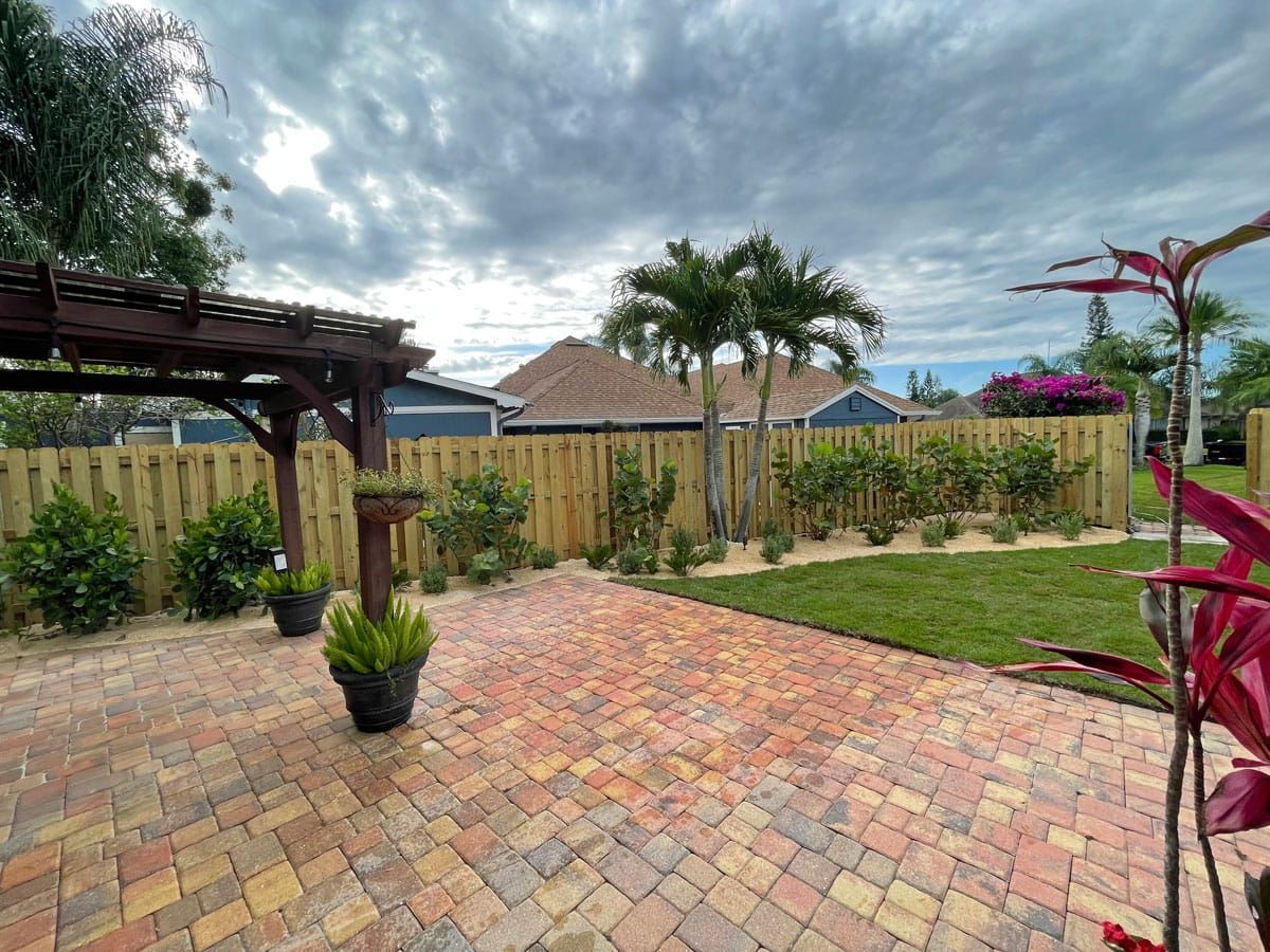 A backyard with a wooden fence and a brick patio.
