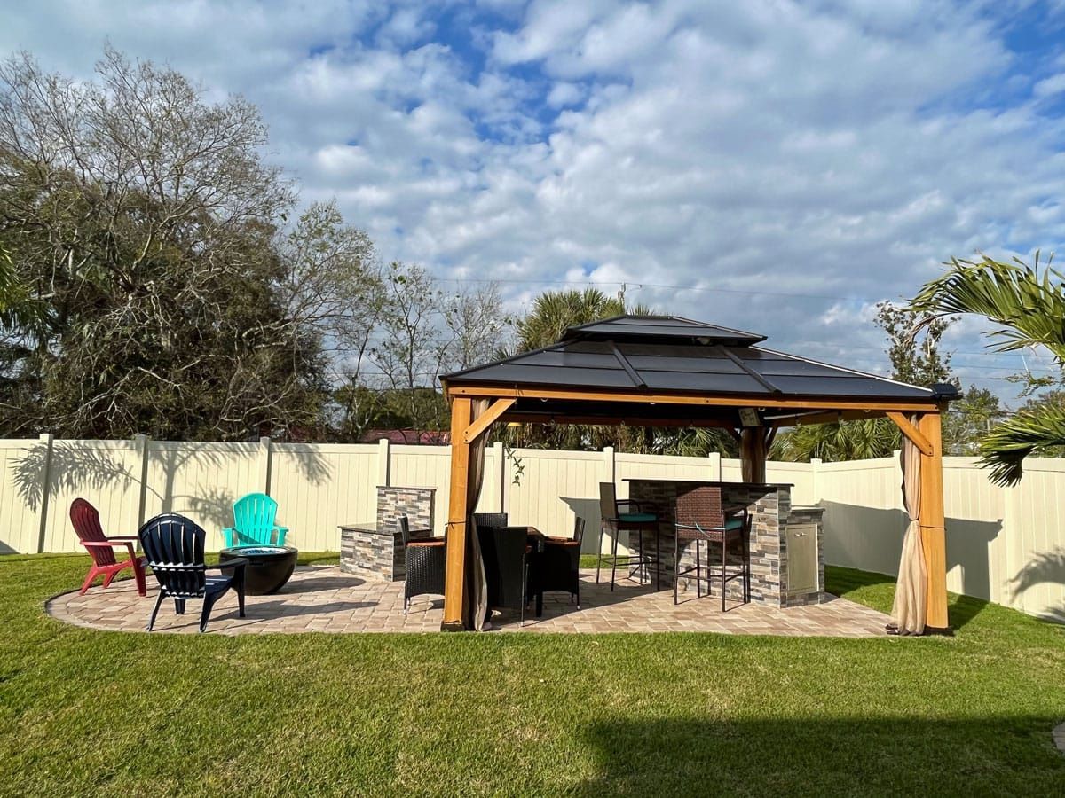 There is a gazebo in the backyard with a fire pit and chairs.