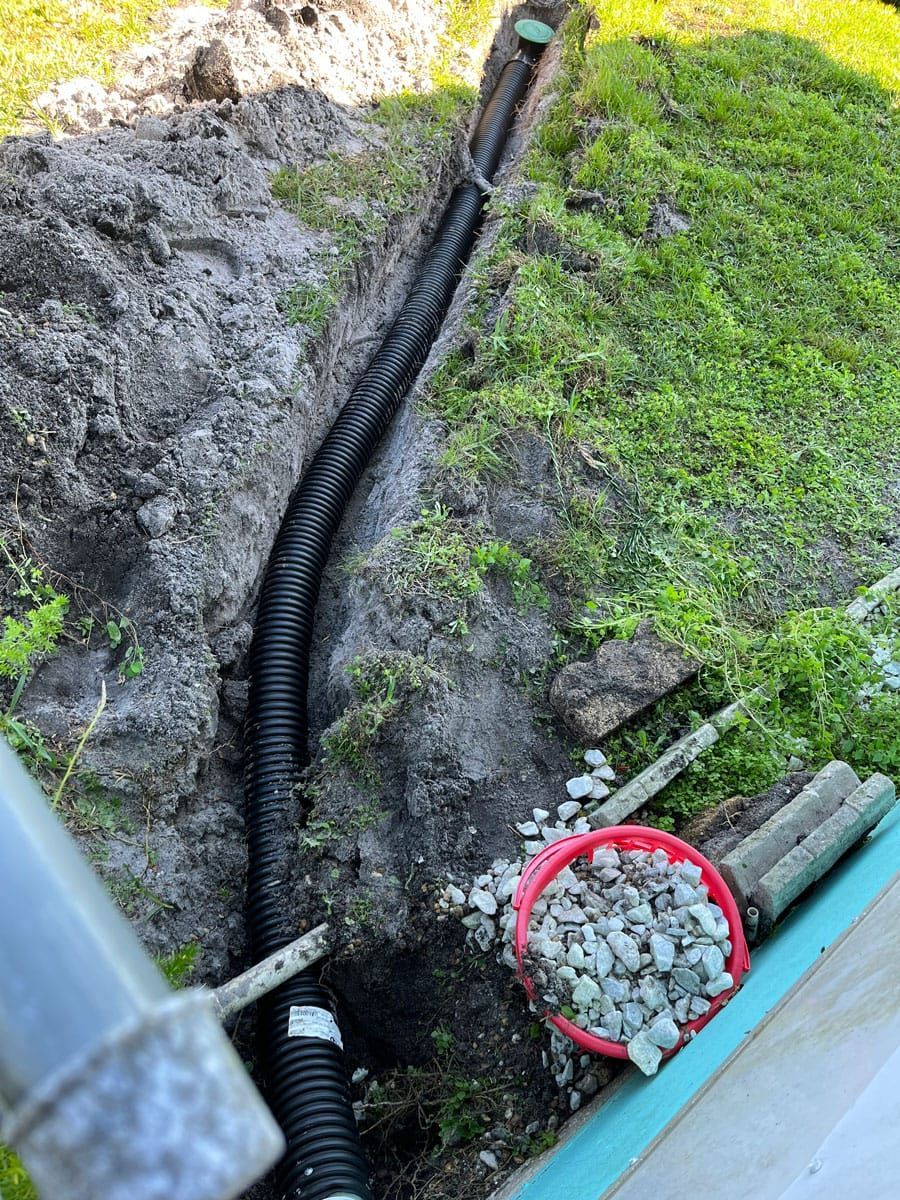 A drain pipe is being installed in the ground next to a bucket of gravel.