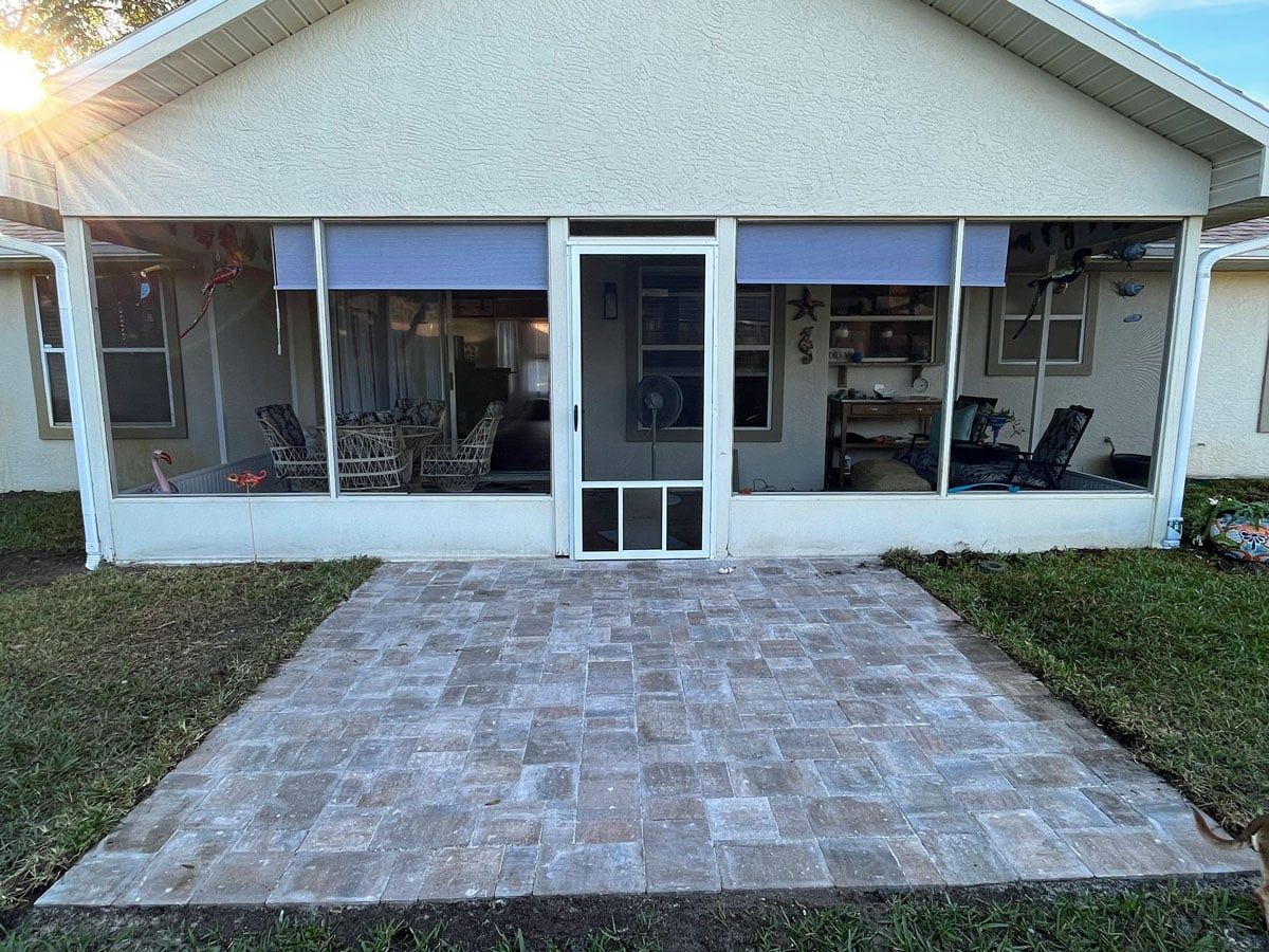 A house with a screened in porch and a patio in front of it.