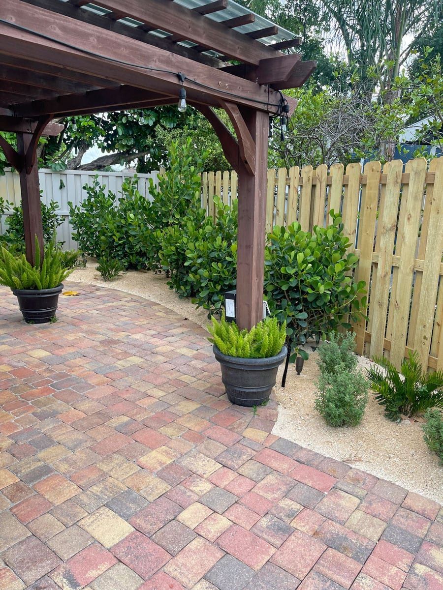 A brick patio with potted plants under a pergola and a wooden fence.