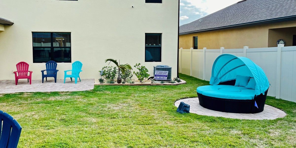 A backyard with a blue day bed , chairs , and a white fence.