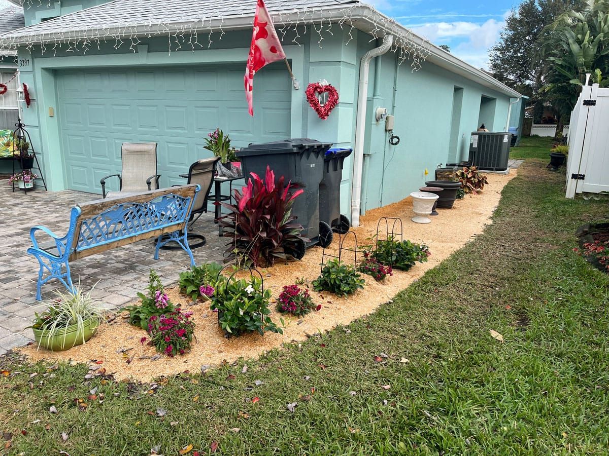 A house with a blue bench , chairs , trash cans and flowers in front of it.
