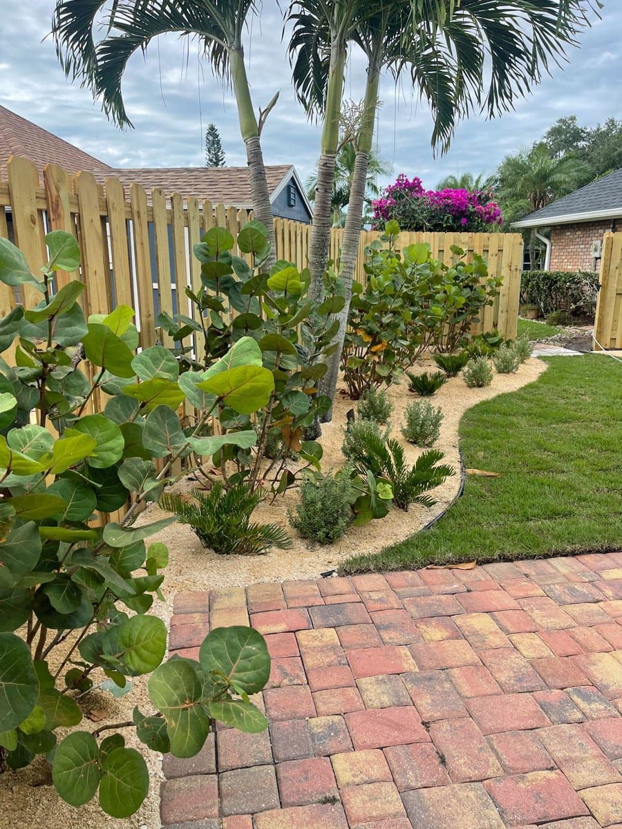 A backyard with a wooden fence , brick walkway , and lots of plants.