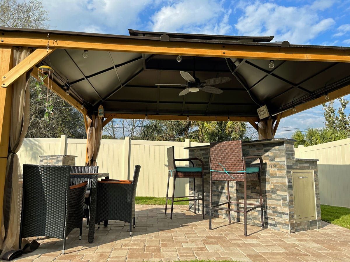 A gazebo with a ceiling fan and a table and chairs underneath it.