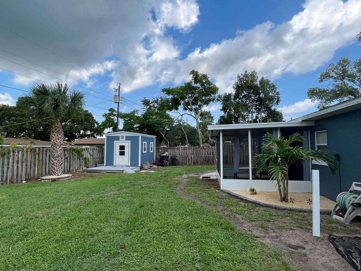 A house with a screened in porch and a shed in the backyard.