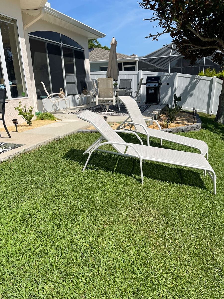 Two lounge chairs are sitting in the grass in front of a house.