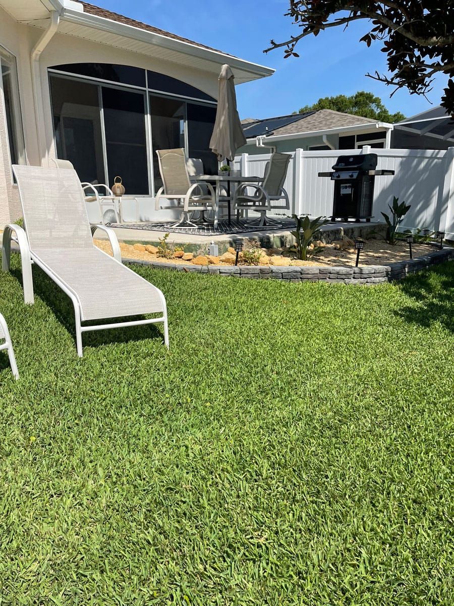 A backyard with lawn chairs and a grill in front of a house.