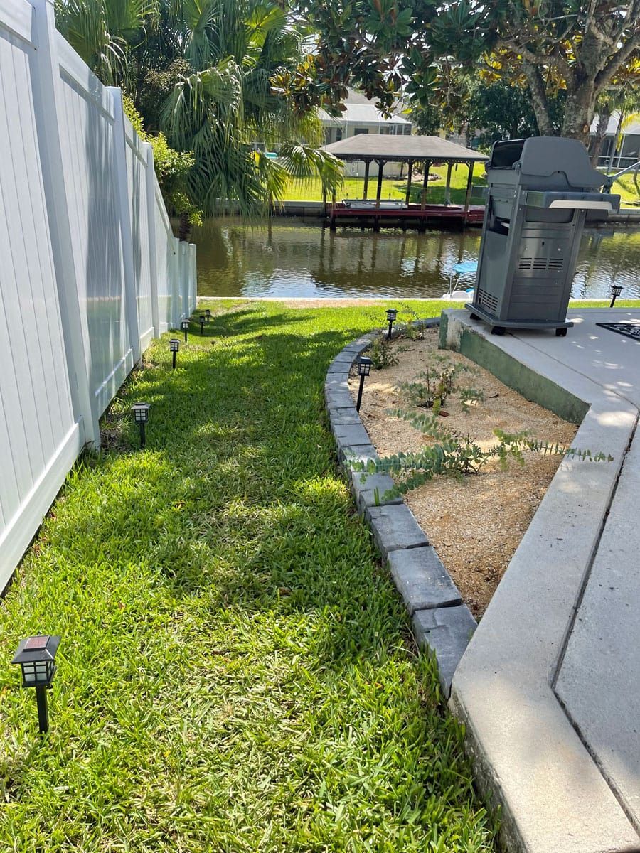 A white fence surrounds a lush green lawn next to a body of water.