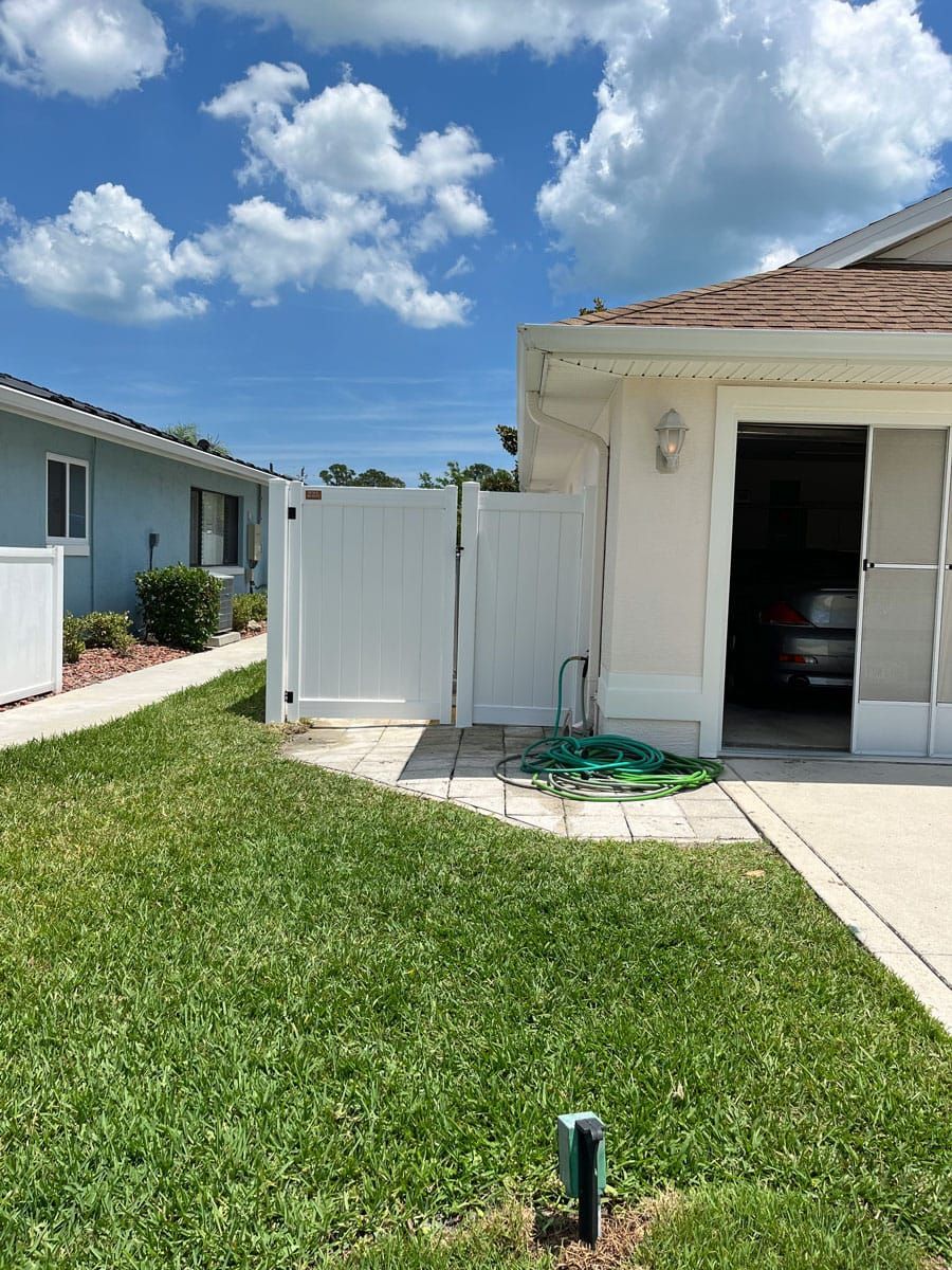 A white house with a white fence and a car parked in the garage.
