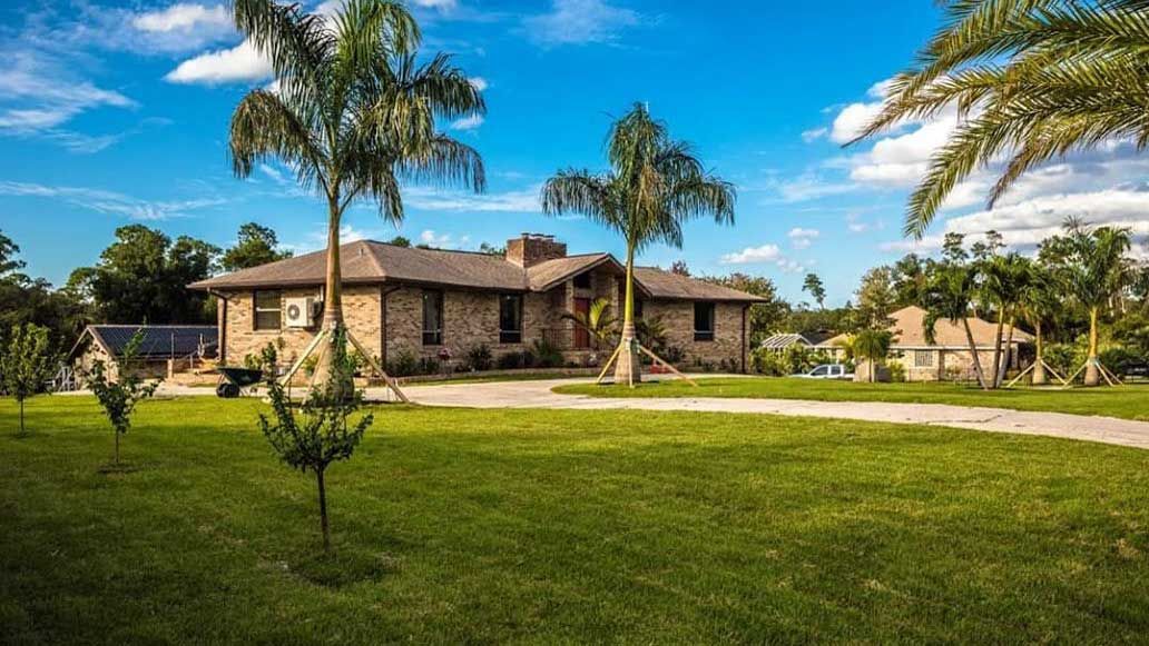 A large house with a lot of grass and palm trees in front of it.
