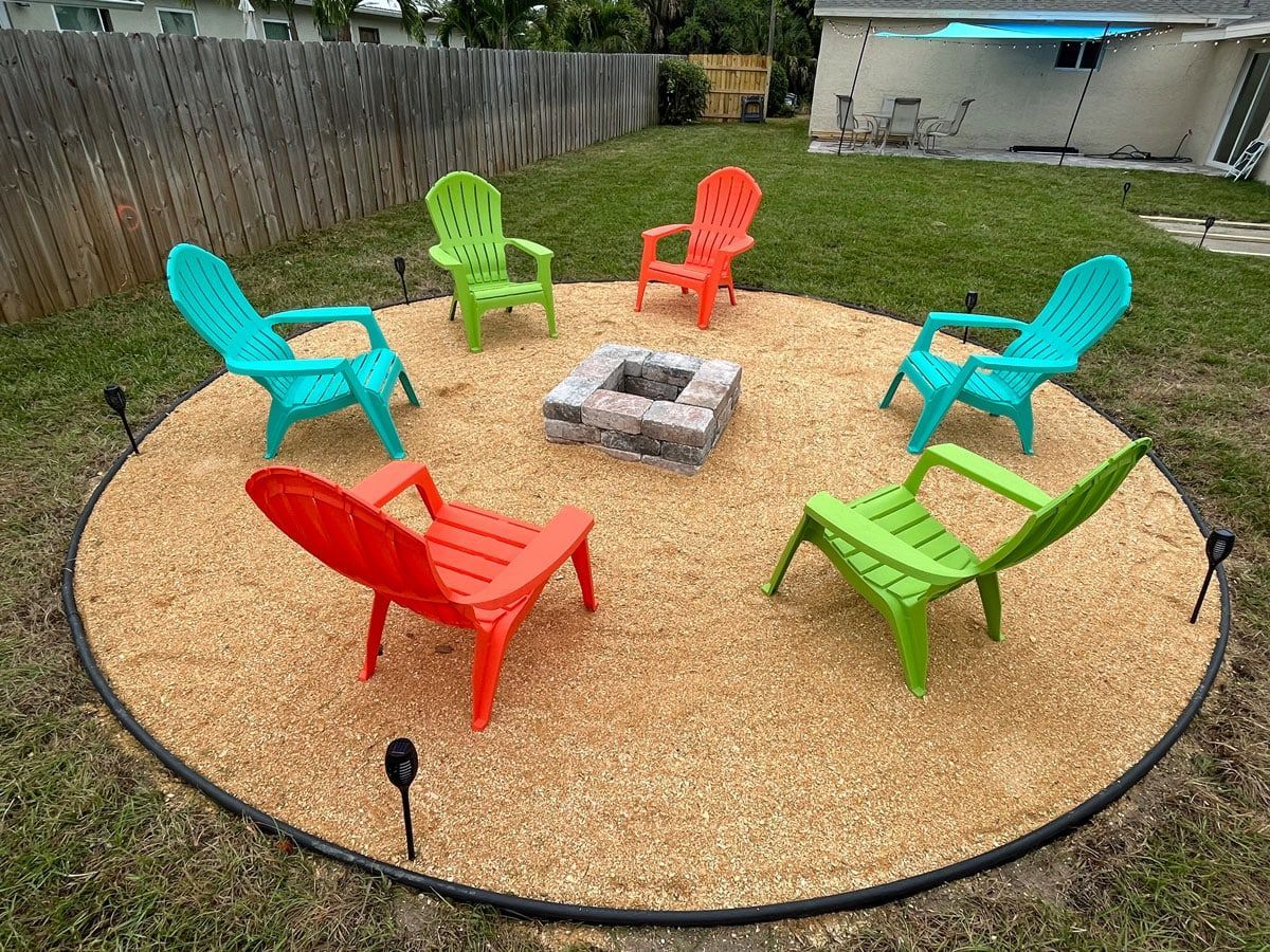 A group of colorful chairs are sitting around a fire pit in a backyard.