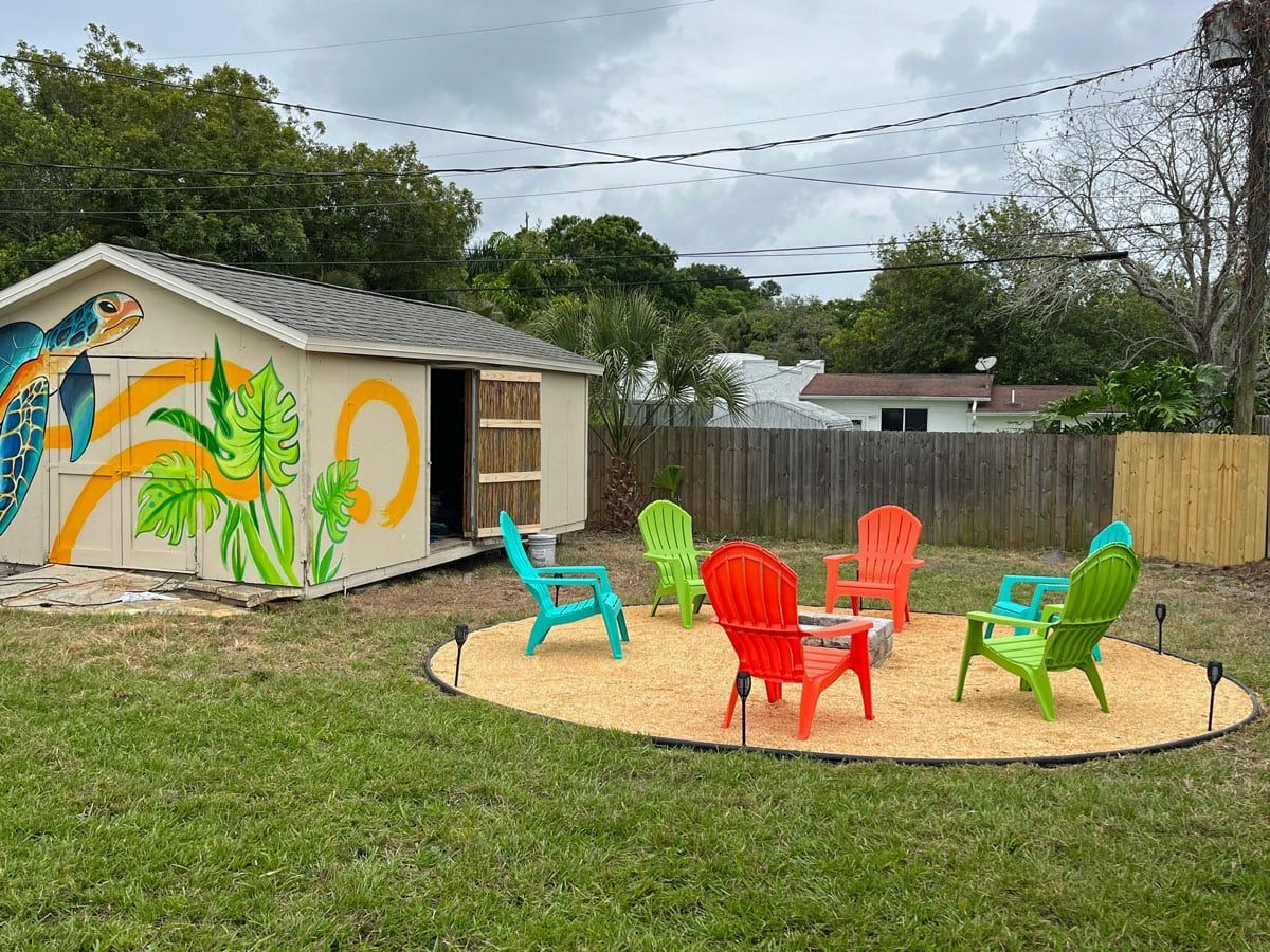 A group of colorful chairs are sitting around a fire pit in a backyard.