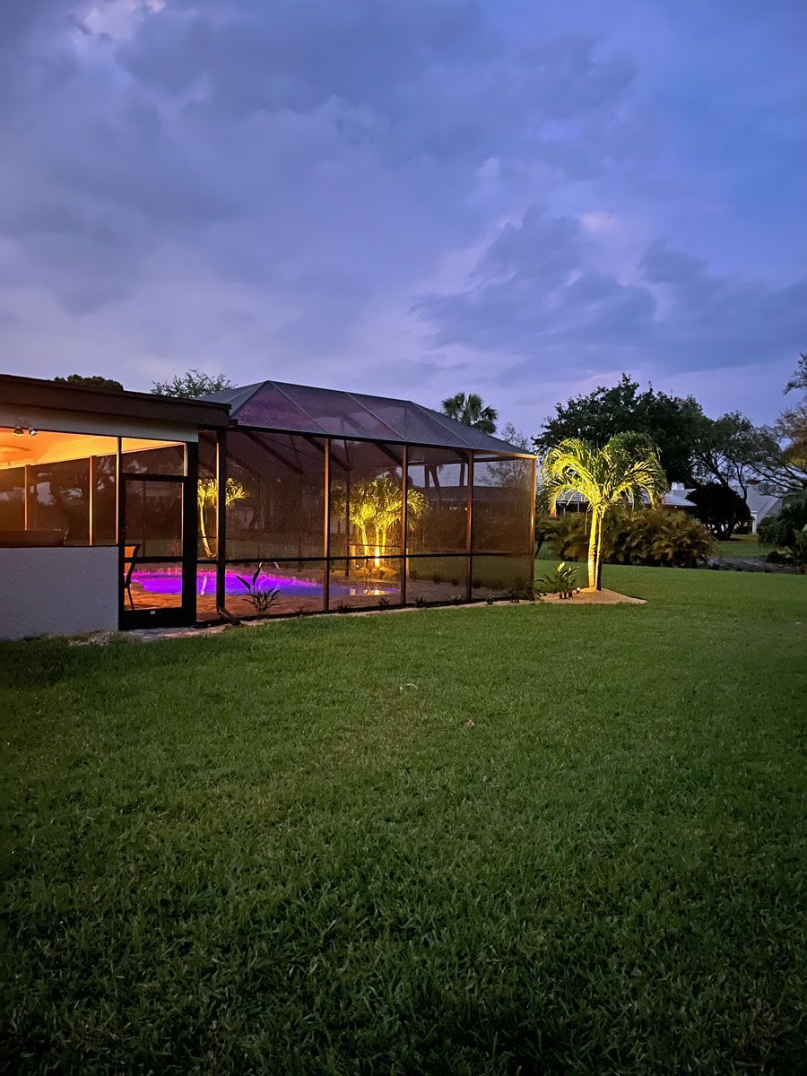 A house with a screened in porch and a swimming pool at night.
