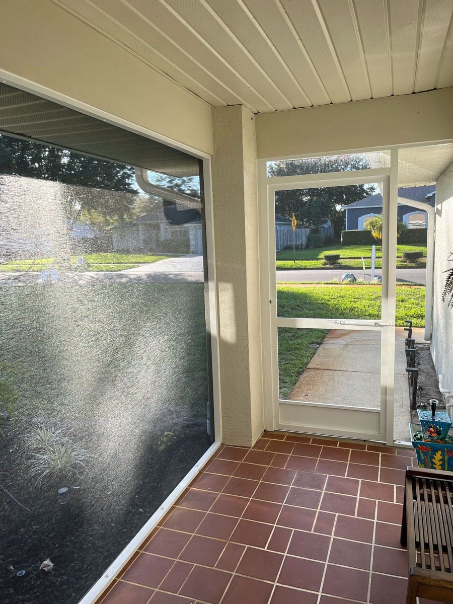A screened in porch with a large window and a tiled floor.