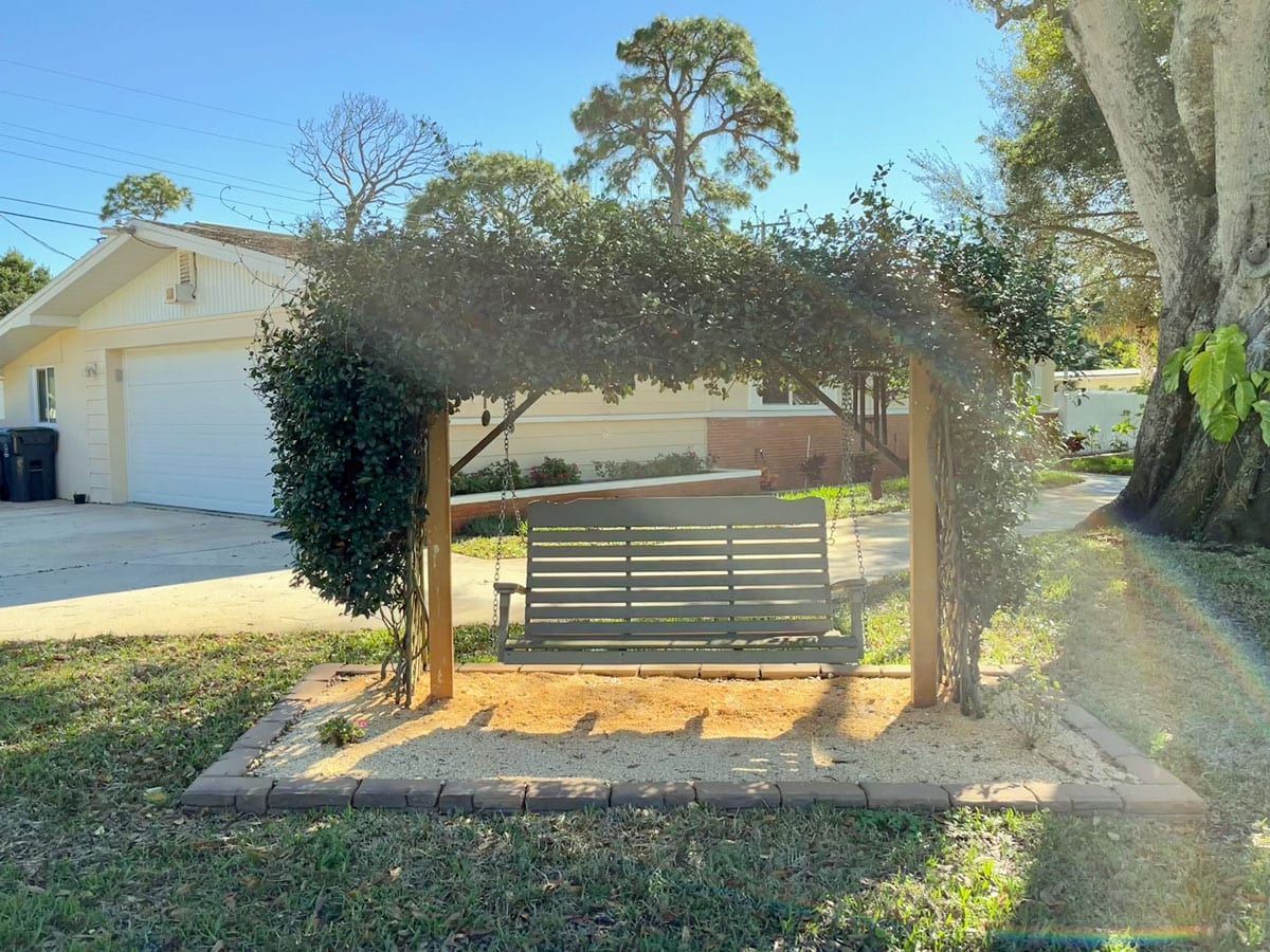A wooden swing under a tree in front of a house