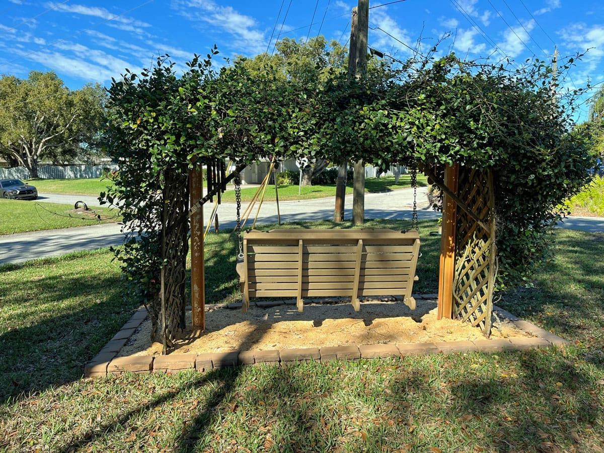 A wooden swing is sitting under a tree in a park.