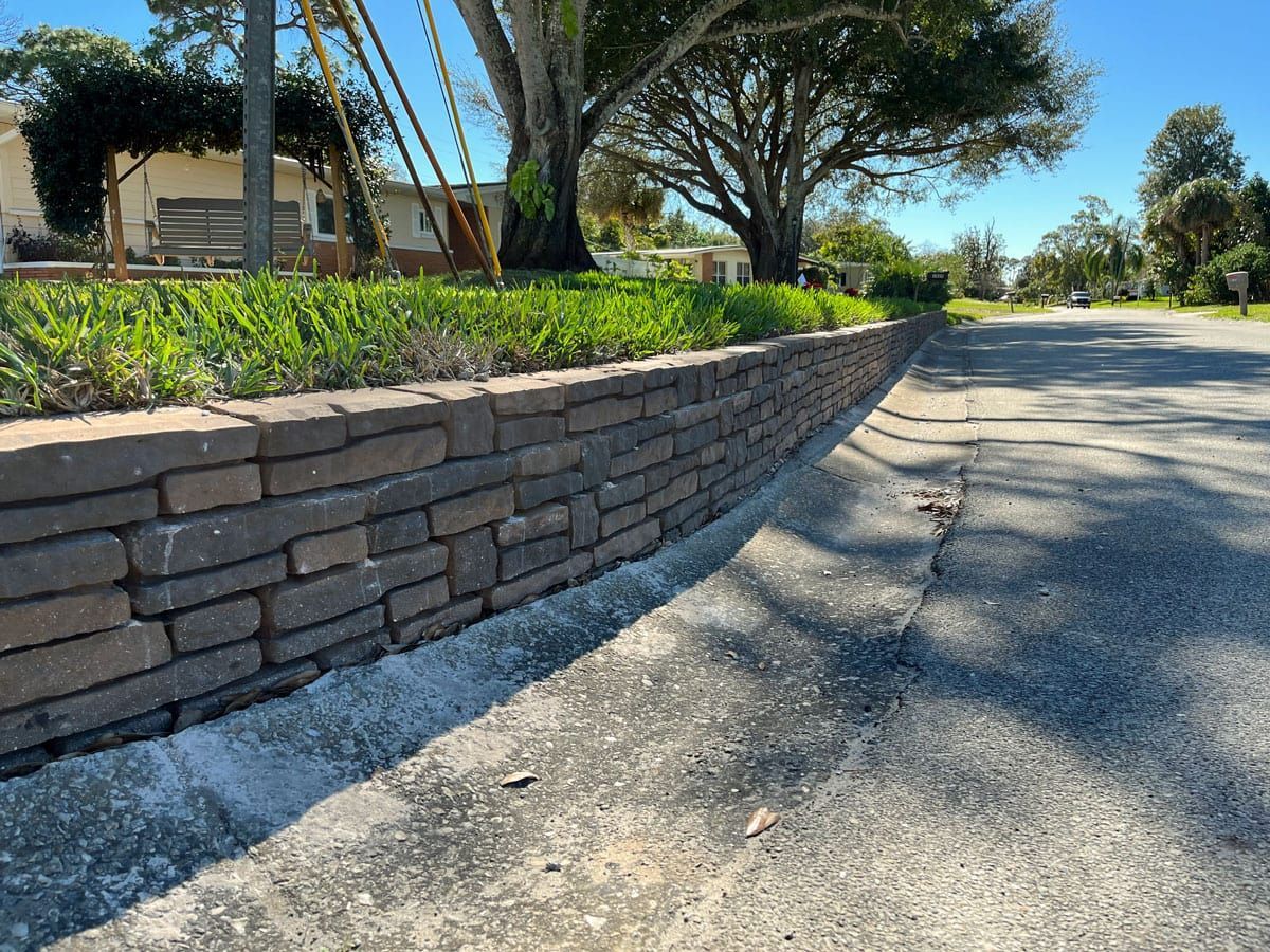 A brick wall along the side of a road next to a tree.