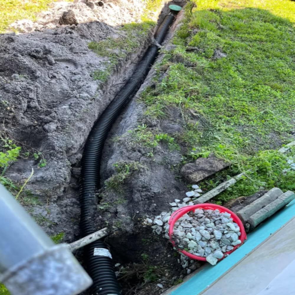 A drain pipe is being installed in the ground next to a bucket of rocks.