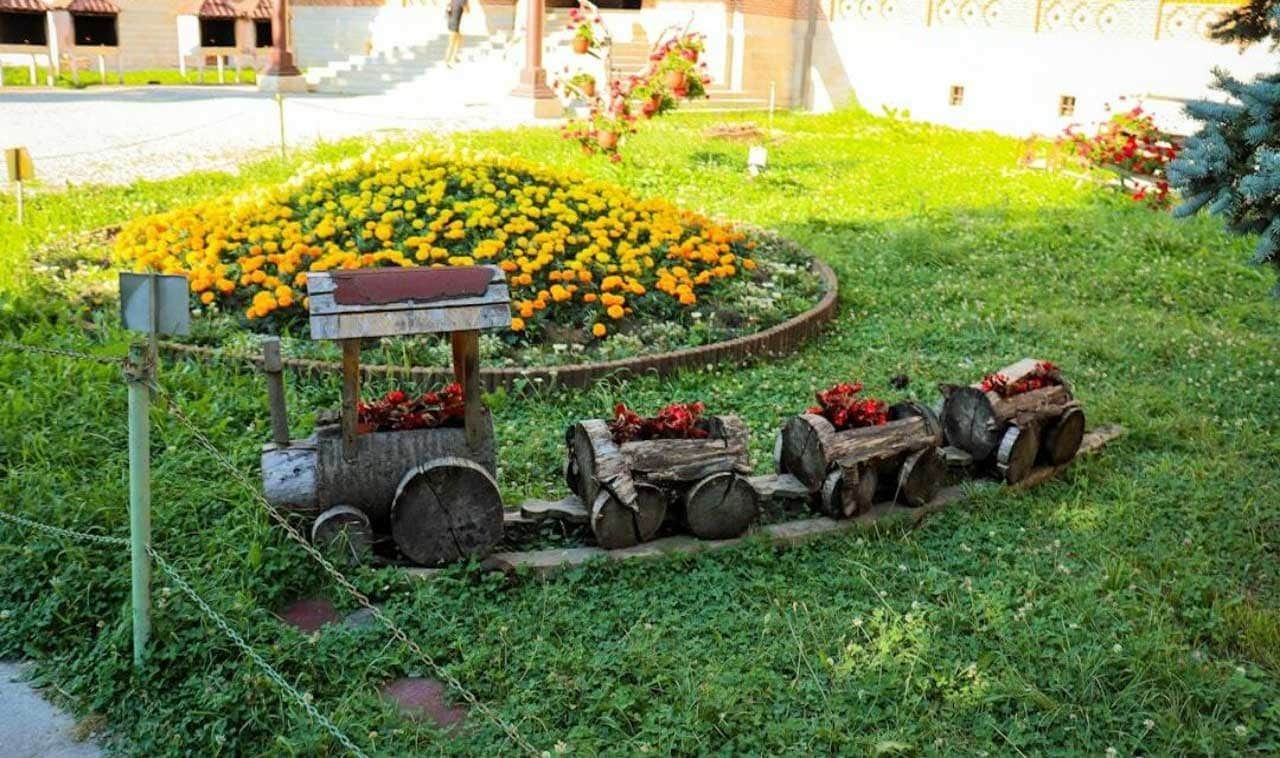 Wooden train flower planter in a grassy yard, with a flower bed of yellow blooms in the background.