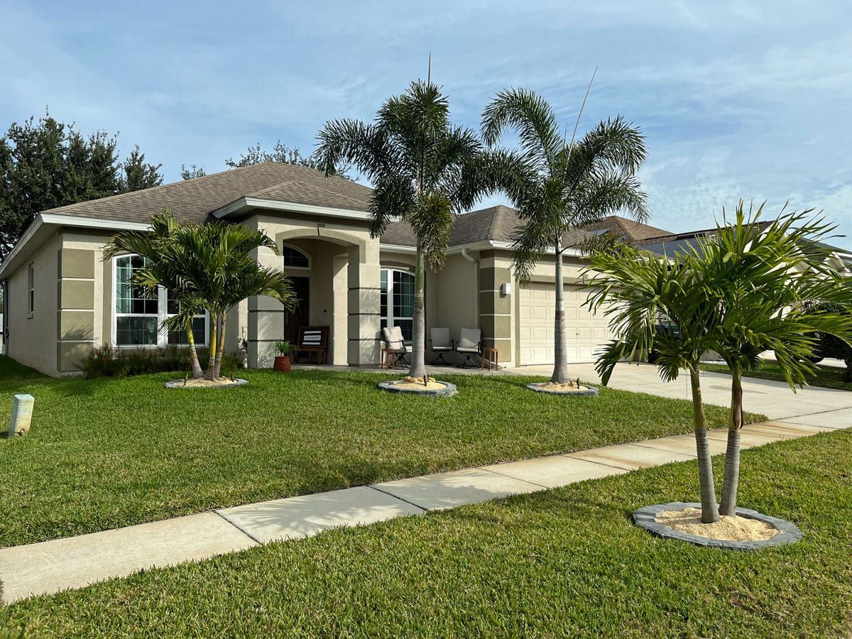A house with a lush green lawn and palm trees in front of it.