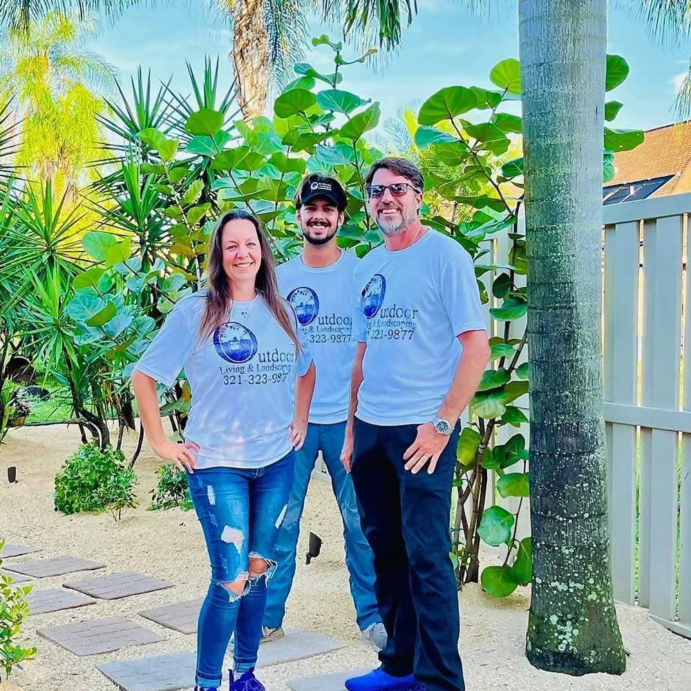 Three people are posing for a picture in front of a palm tree.