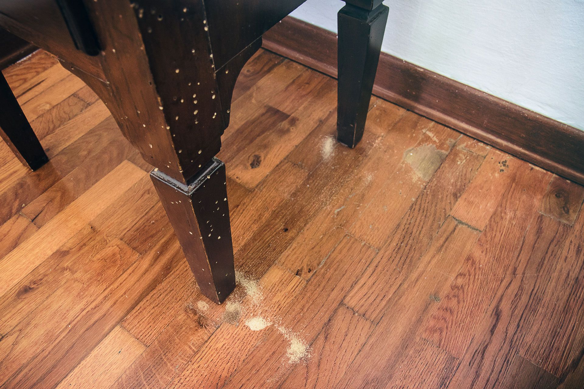 Wooden table with termite damage, near a baseboard on a hardwood floor.
