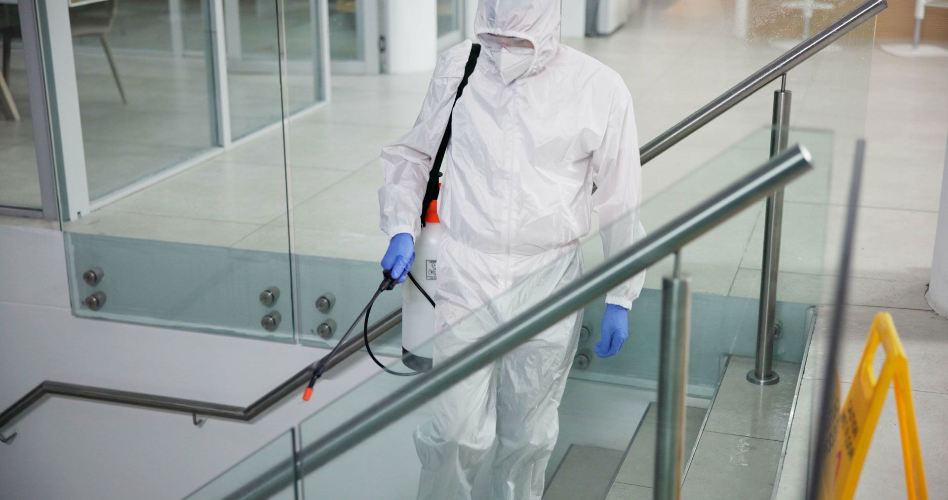 Person in hazmat suit sanitizing stairs with a sprayer in an office building.