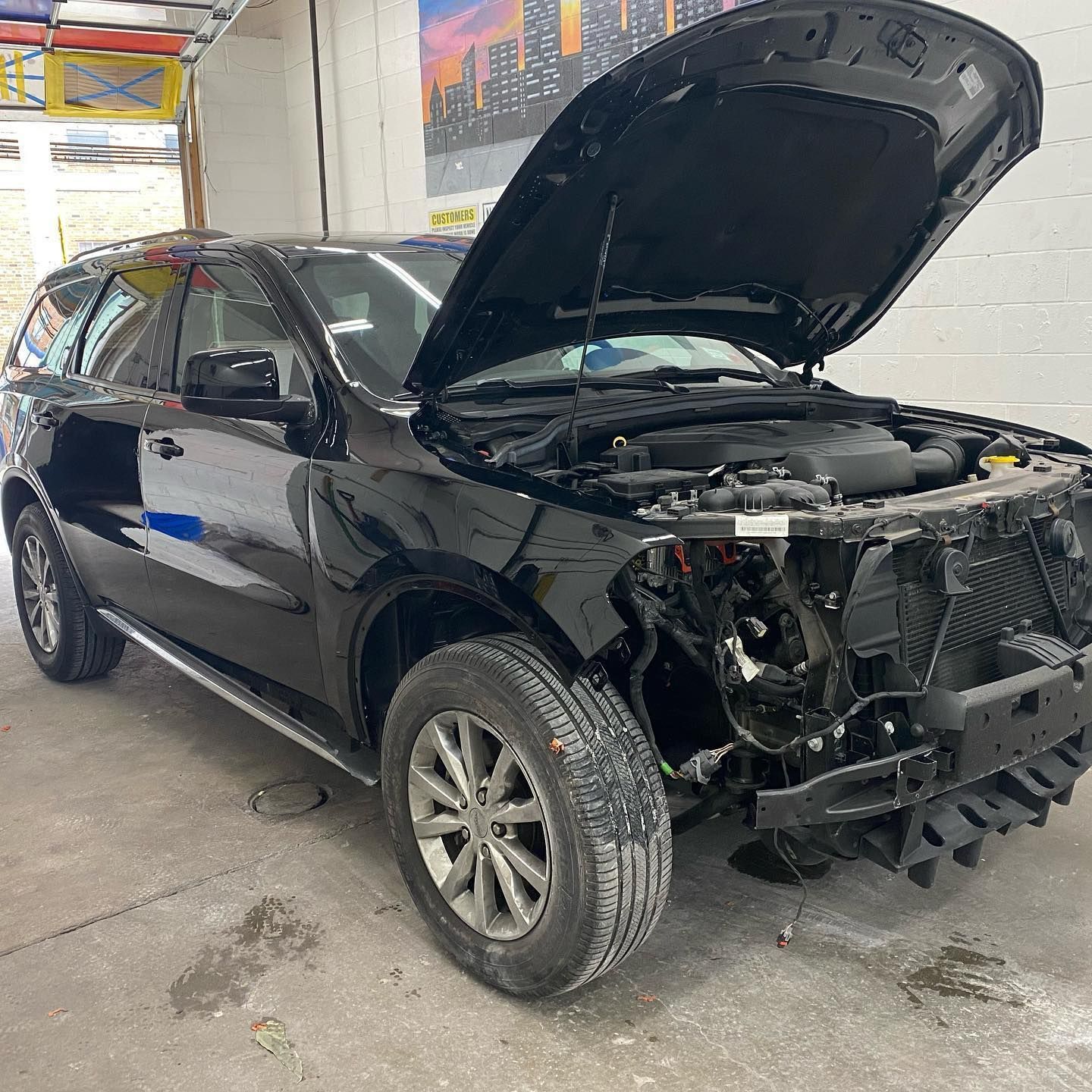 A black car with the hood open is parked in a garage.