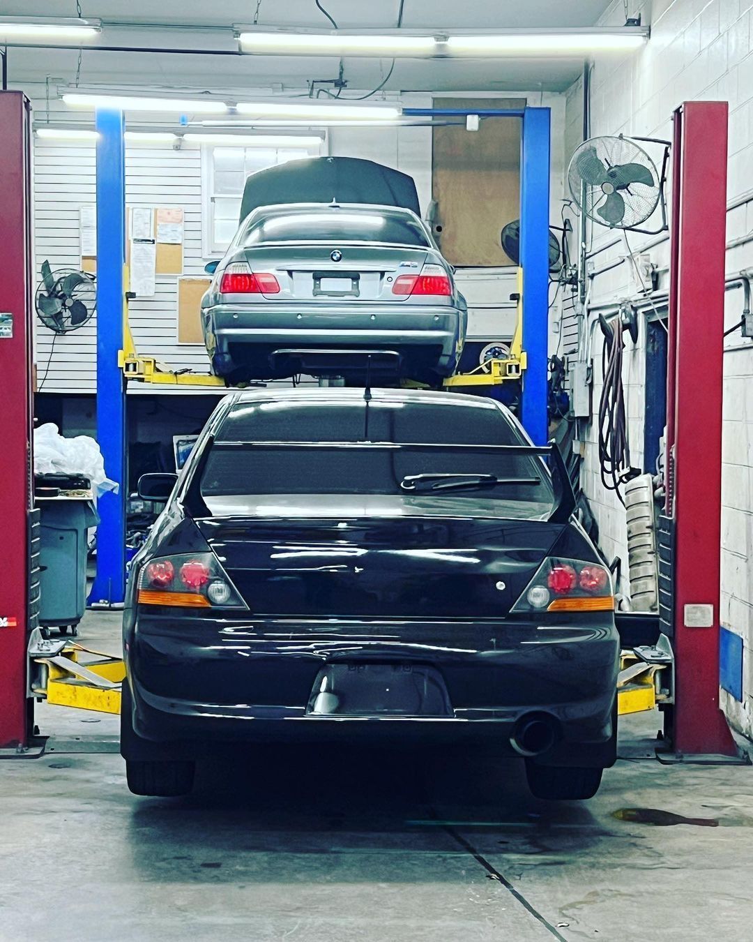 Two cars are sitting on a lift in a garage