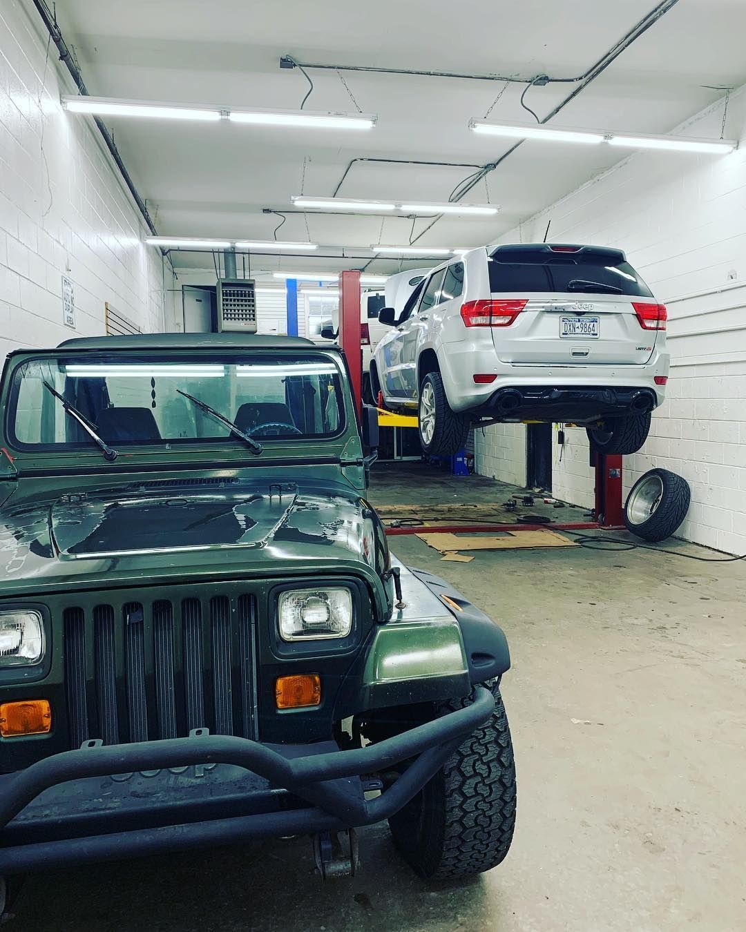 A green jeep is parked next to a white suv in a garage.