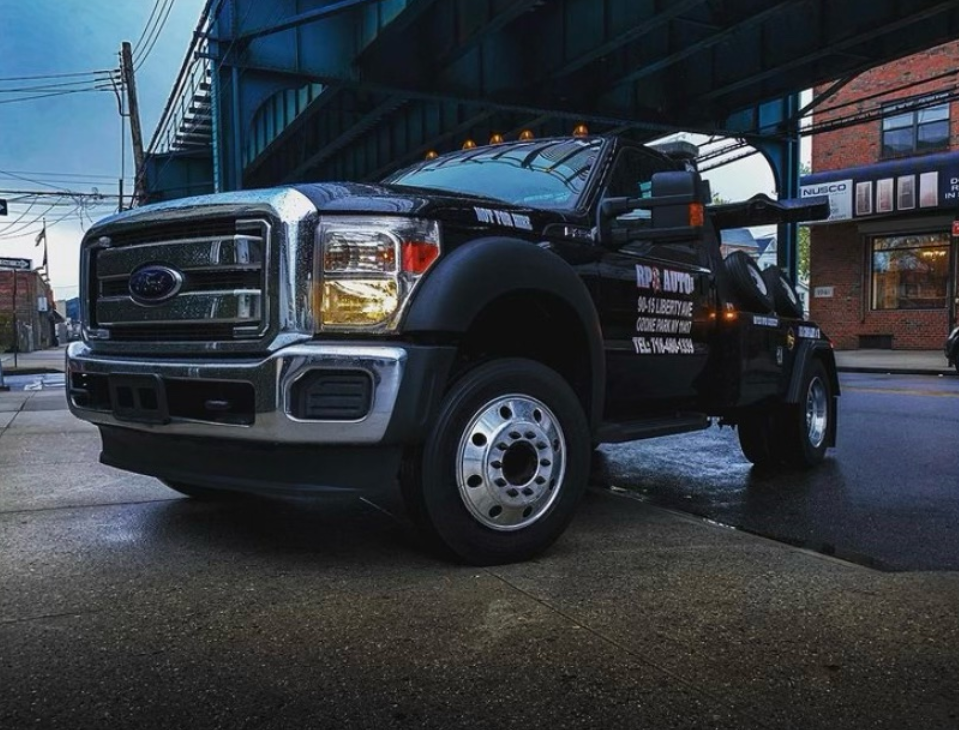 A black ford tow truck is parked under a bridge